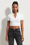 a woman wearing a white, short-sleeved, zip-front crop top paired with dark-washed jeans