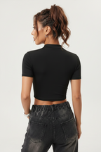 a woman wearing a black, short-sleeved, zip-front crop top paired with dark-washed jeans