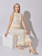 Woman wearing a white crochet dress sitting on a white block against a light gray background