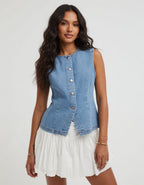 Woman wearing a denim vest over a white dress on a plain background