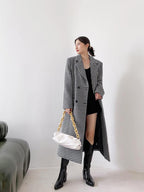 Woman wearing a long houndstooth coat holding a white handbag against a plain background