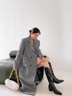 Woman wearing a long houndstooth coat and black knee-high boots sitting on a green couch.