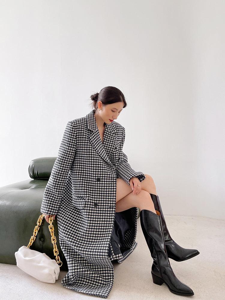 Woman wearing a long houndstooth coat and black knee-high boots sitting on a green couch.