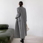 Person wearing a long black and white checkered coat standing in a minimalistic room.