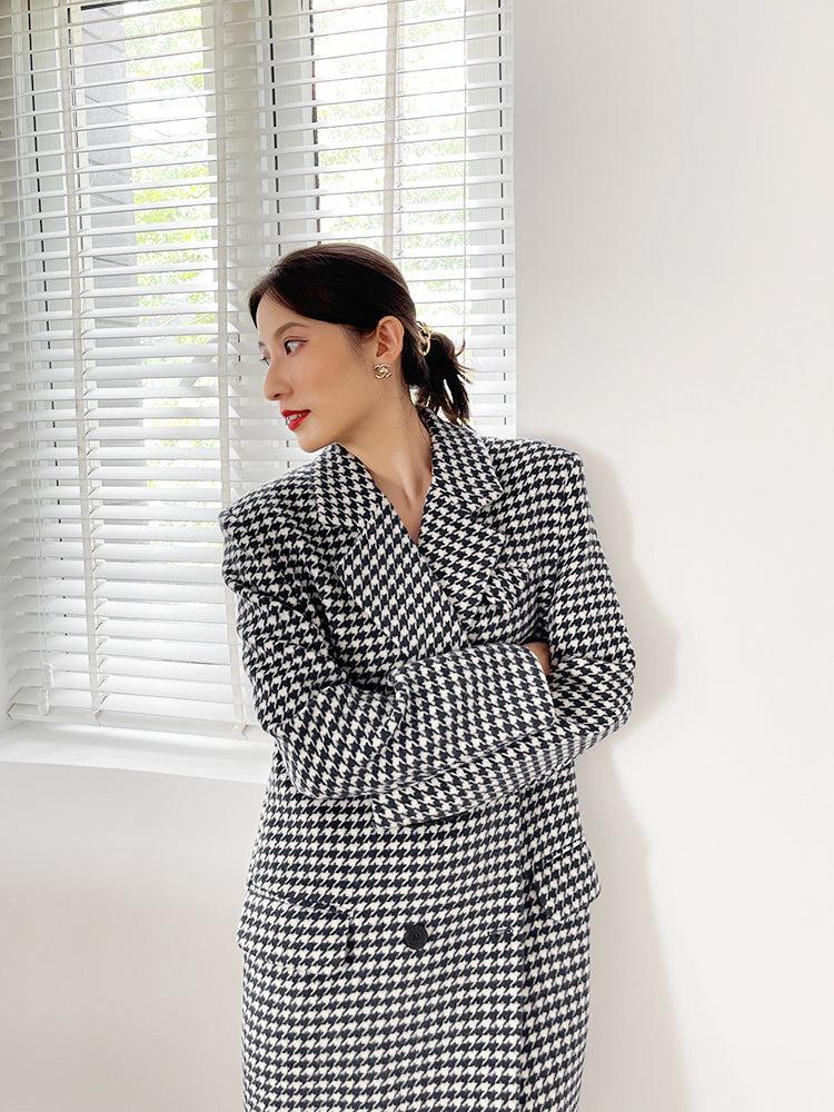 Woman wearing a black and white checkered suit standing in front of a window with blinds.