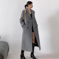 Woman wearing a long houndstooth coat with a plain background