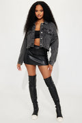 Woman wearing a denim jacket, black leather skirt, and knee-high boots on a white background
