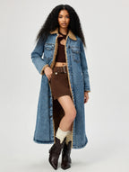 Woman wearing a long denim coat with a white background