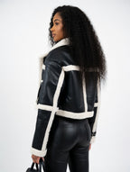 Woman wearing a black leather jacket with white shearling trim on a white background