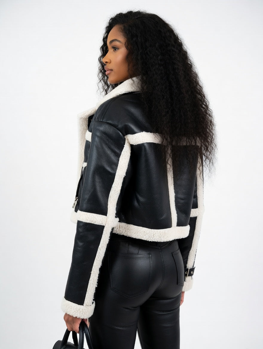 Woman wearing a black leather jacket with white shearling trim on a white background