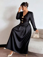 Woman wearing a black dress with gold buttons, holding a white handbag indoors.