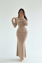 Woman wearing a beige long-sleeve dress taking a mirror selfie in a white background.