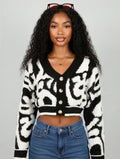 Woman wearing a black and white patterned cardigan with blue jeans on a gray background