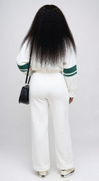 Person wearing a white sweater with green accents and white pants, standing against a plain background.