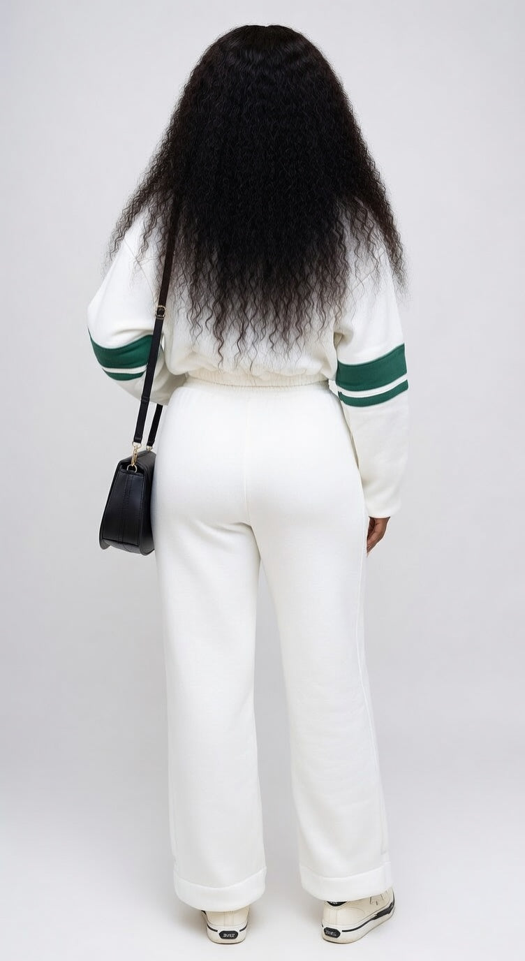 Person wearing a white sweater with green accents and white pants, standing against a plain background.