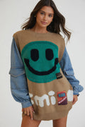 Woman wearing a unique sweater with a smiley face design and denim jacket.