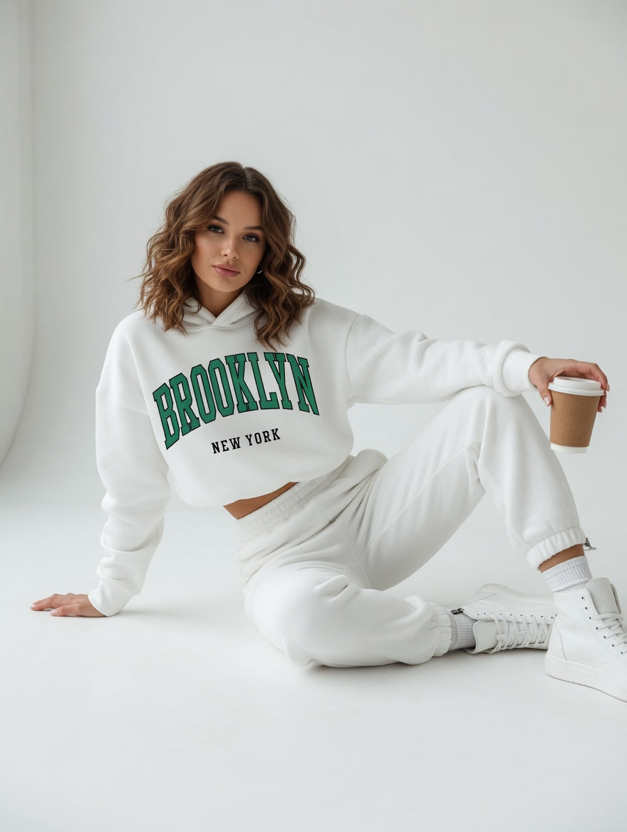 Woman wearing a white hoodie with 'Brooklyn New York' text, sitting on a light gray floor.