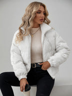Woman wearing a white ribbed knit jacket over a beige top, sitting against a plain background.
