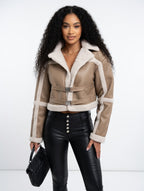 Woman wearing a beige shearling jacket with white trim on a white background