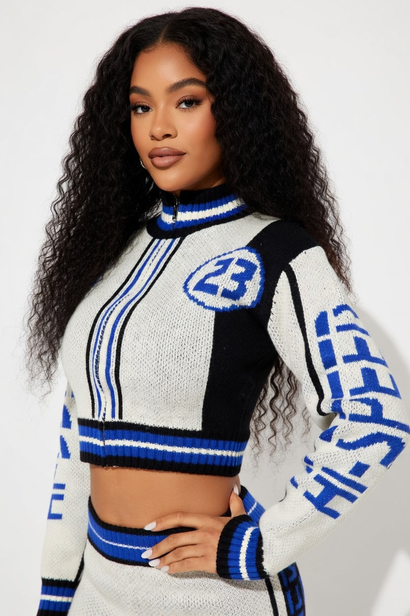 Woman wearing a black, white, and blue sweater with number 23 design on a plain background