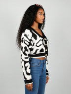 Woman wearing a black and white patterned cardigan with blue jeans on a gray background