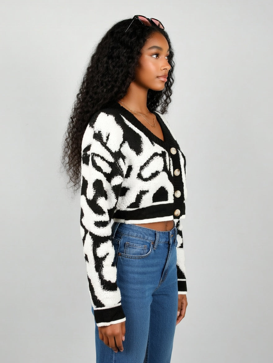 Woman wearing a black and white patterned cardigan with blue jeans on a gray background