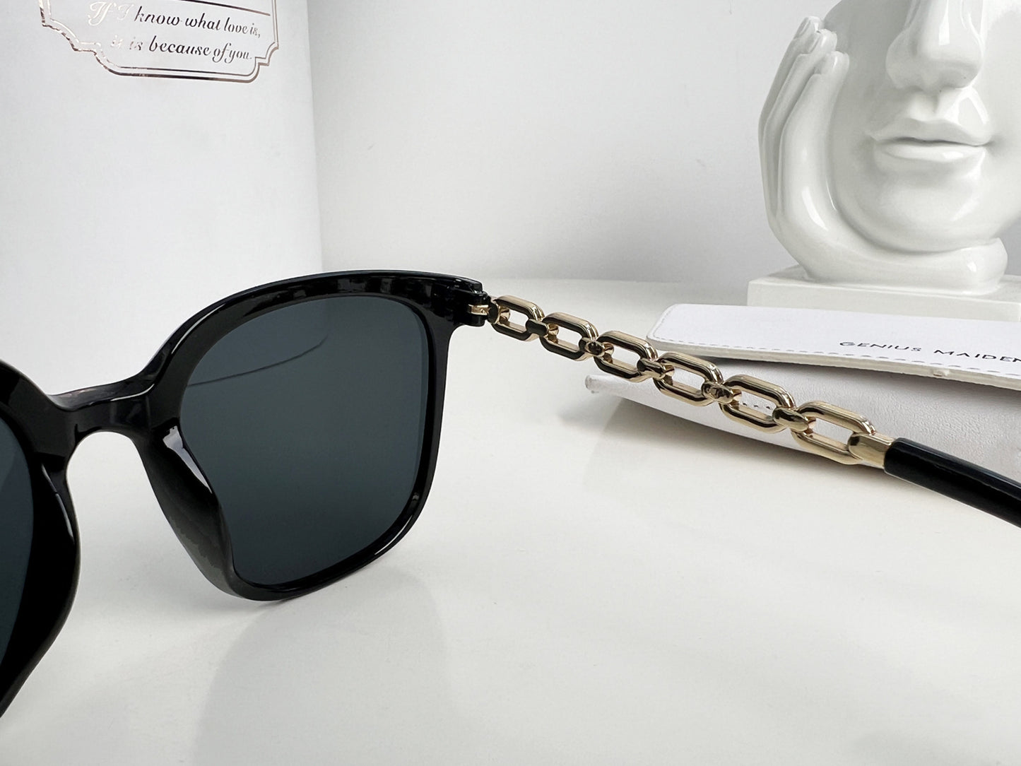 Black sunglasses with a gold chain on a white surface