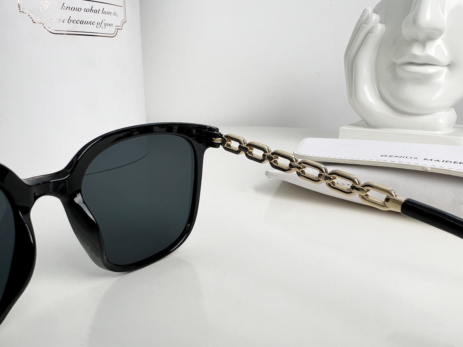 Black sunglasses with a gold chain on a white surface