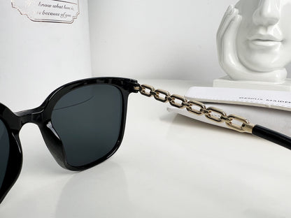 Black sunglasses with a gold chain on a white surface