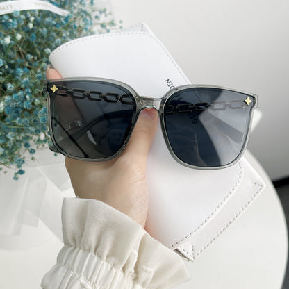 Sunglasses with chain detail held by a hand against a blurred background
