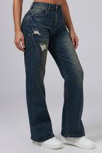 Person wearing blue jeans with a slight distressed look on a plainbackground