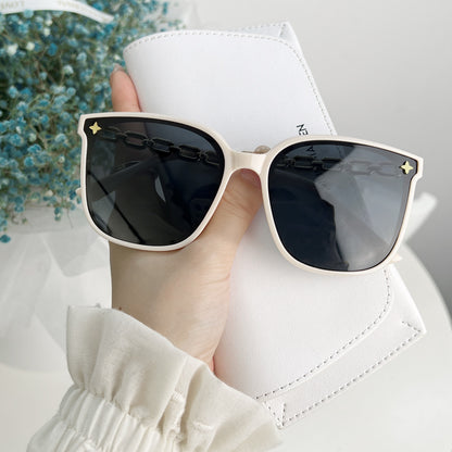 Sunglasses with gold chain design held by a hand against a blurred background