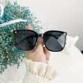 Black sunglasses held by a hand with a blurred background of blue flowers and a white surface.