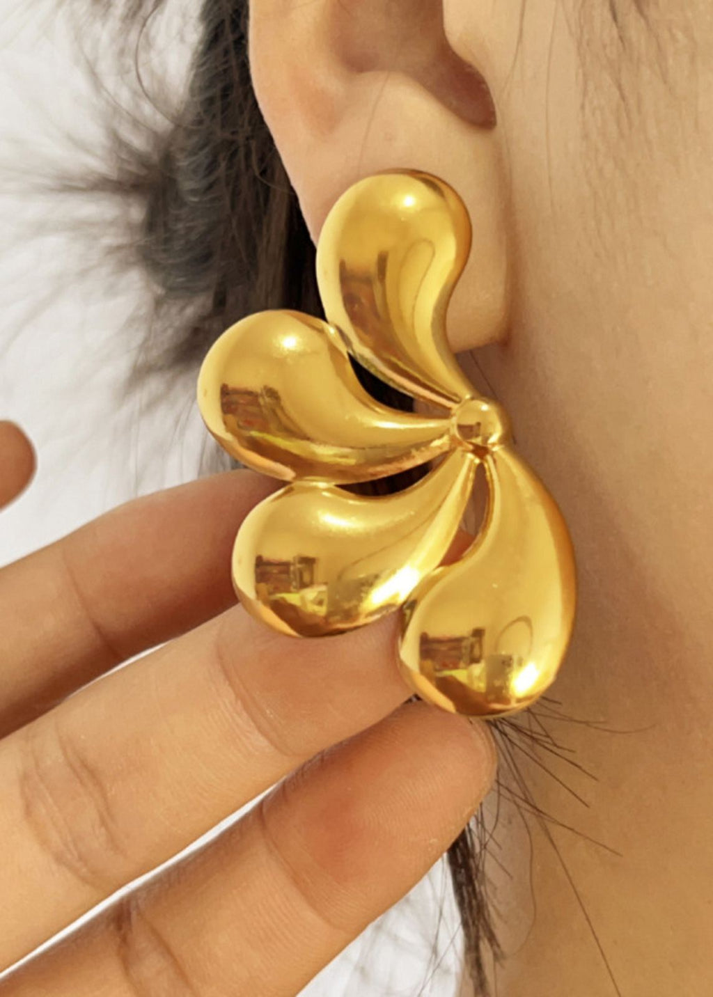 Gold floral earring worn by a person with a blurred background
