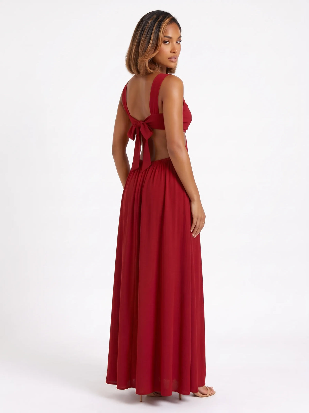 The dress shown is a crimson red maxi dress featuring side cutouts at the waist, a structured sweetheart bustier top with gathered drape detail, wide shoulder straps, and a bow tie backclosure.