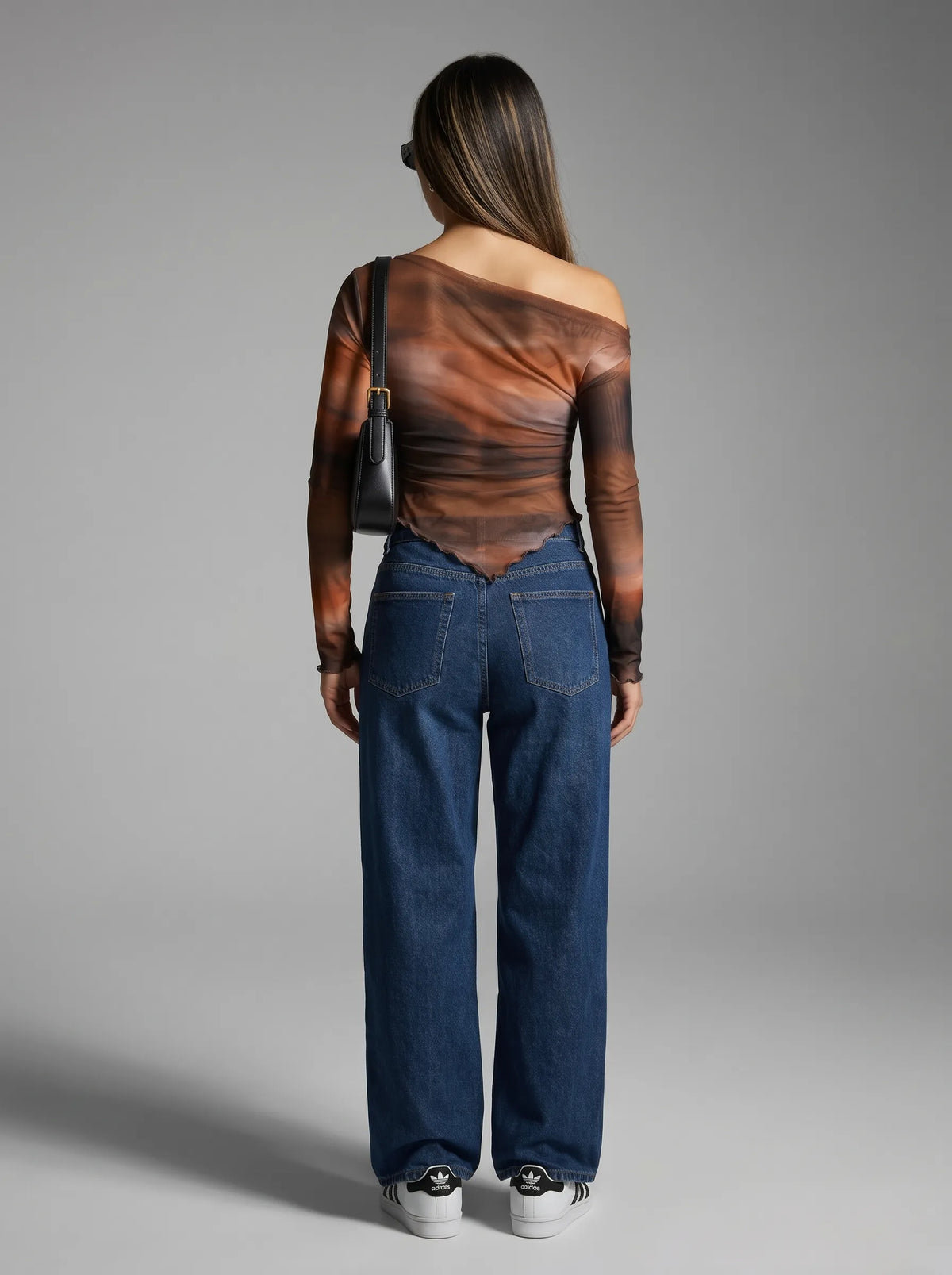 Model wearing a long-sleeved, one-shoulder top is crafted from a sheer, lightweight mesh fabric featuring an abstract, smoky watercolor print in rich tones of warm rust orange, deep brown, and muted charcoal. The fitted, asymmetrical design features soft all-over ruching that contours the body, complemented by a sleek one-shoulder neckline and a uniquely curved, lettuce-edge hemline
