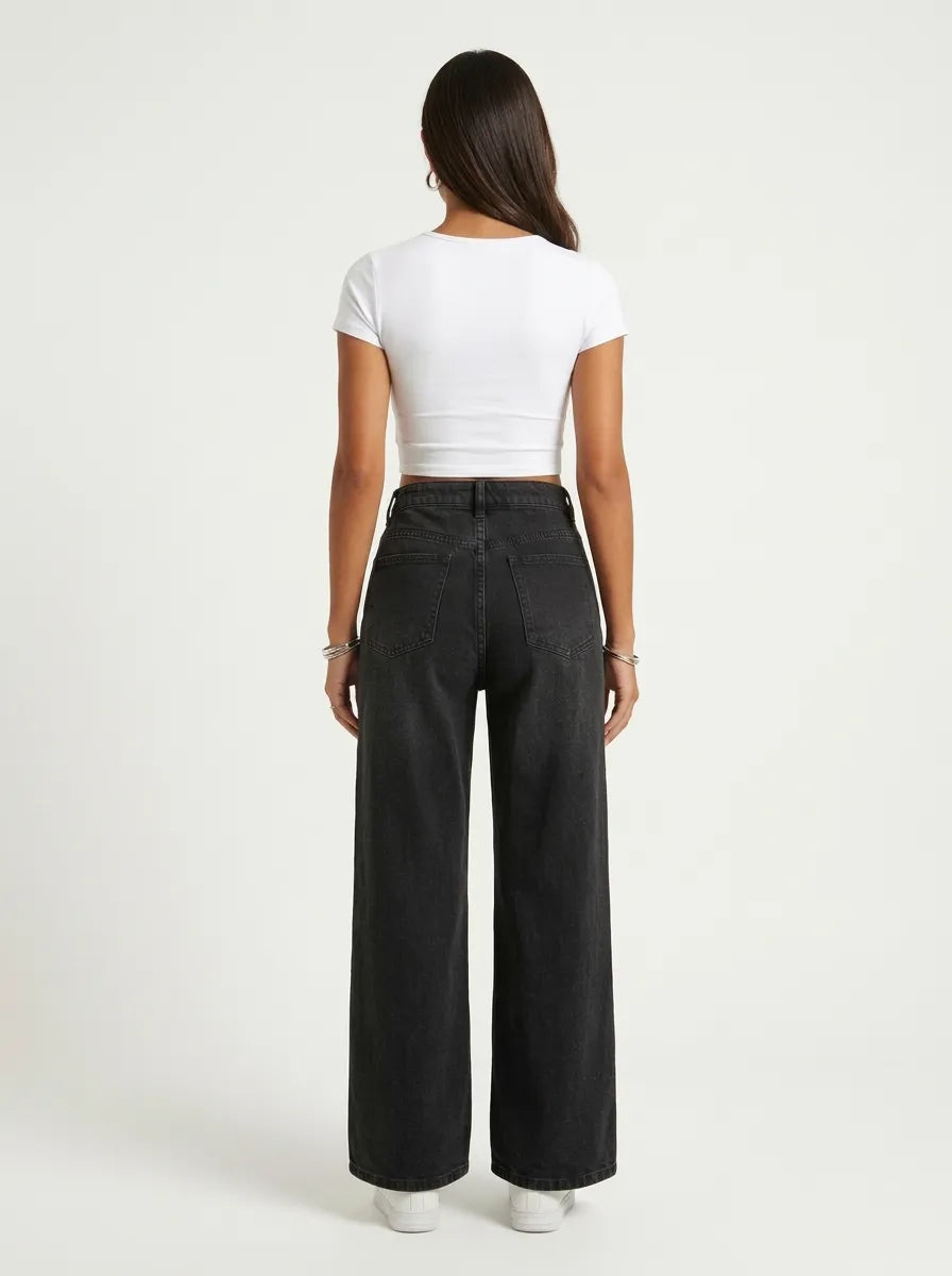 A model wearing a pair of high-waisted, wide-leg jeans is crafted from a dark washed-black or washed-charcoal denim completely covered in a sparkling, all-over pattern of tiny silver rhinestones and crystal studs that scatter densely down the legs. 
