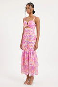 This is a vibrant maxi dress features an all-over abstract watercolor floral print in shades of pink, orange, purple, and yellow on a light background. It is designed with a sweetheart bustier-style top with sweetheart cutout at the center bust, thin shoulder straps, and a front waist cutout.