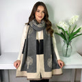 Woman wearing a gray scarf with tree patterns, standing next to a white table with a vase of flowers.