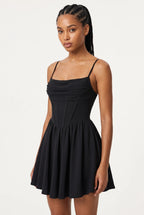 A woman viewed from the back wearing a black spaghetti-strap mini dress with a fitted bodice and flared skirt, against a plain light background.