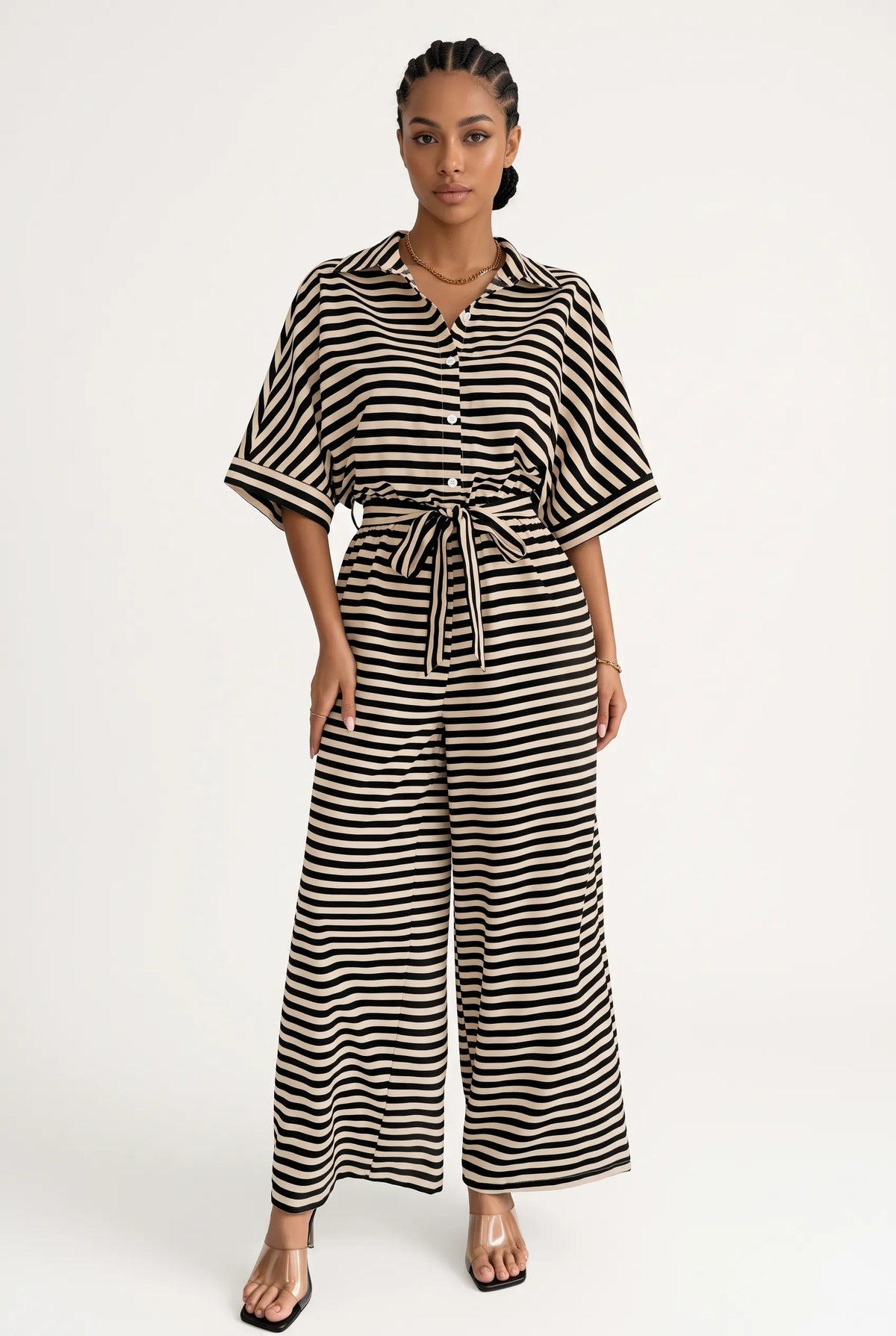 A woman modeling a black and white horizontally striped jumpsuit with a tie waist and wide legs, standing against a plain white studio background.