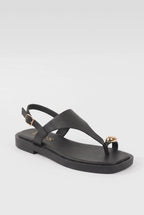 A black leather thong sandal with a low block heel, adjustable ankle strap with a gold buckle, and a small gold heart-shaped embellishment on the toe post, shown against a light gray background.