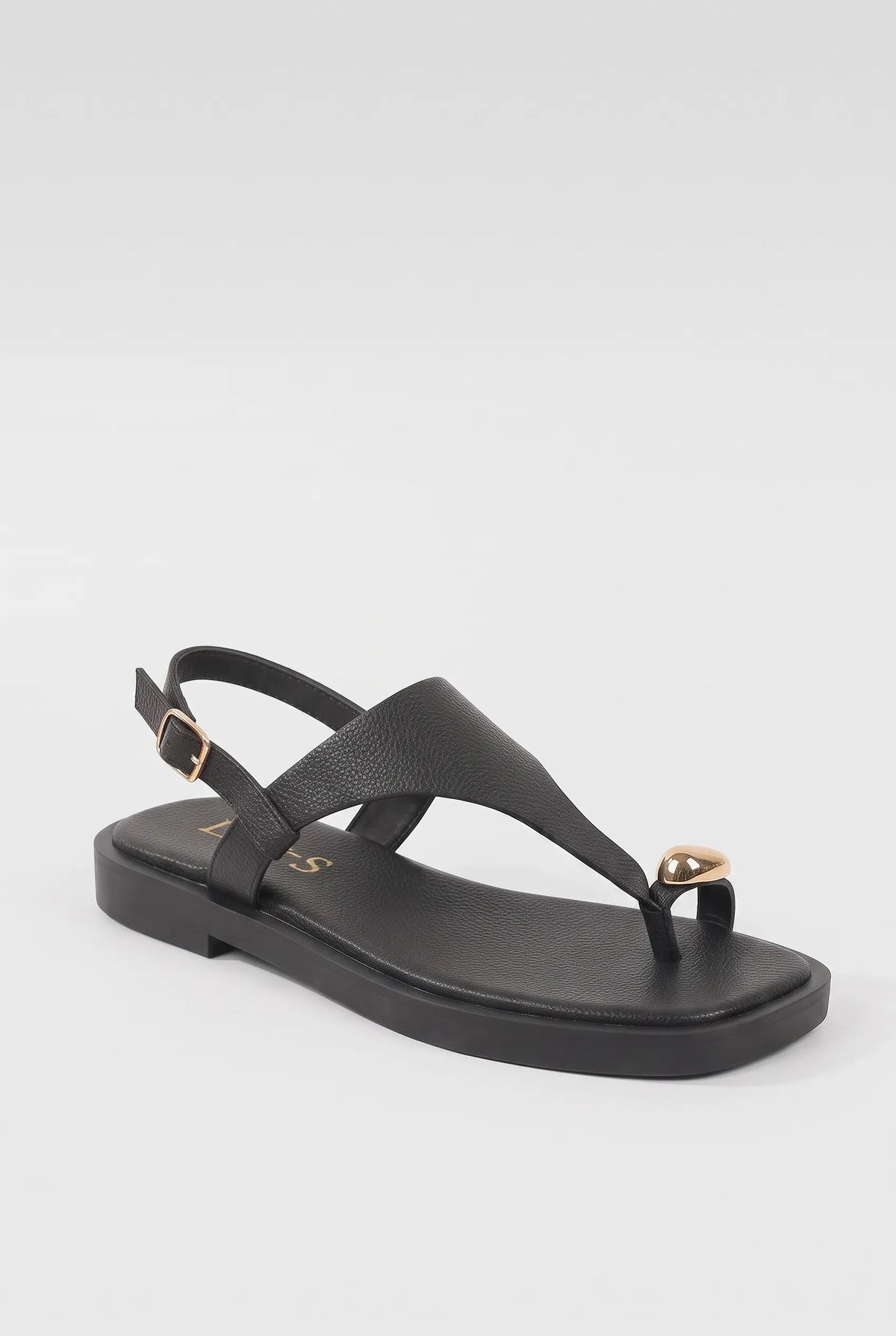 A black leather thong sandal with a low block heel, adjustable ankle strap with a gold buckle, and a small gold heart-shaped embellishment on the toe post, shown against a light gray background.