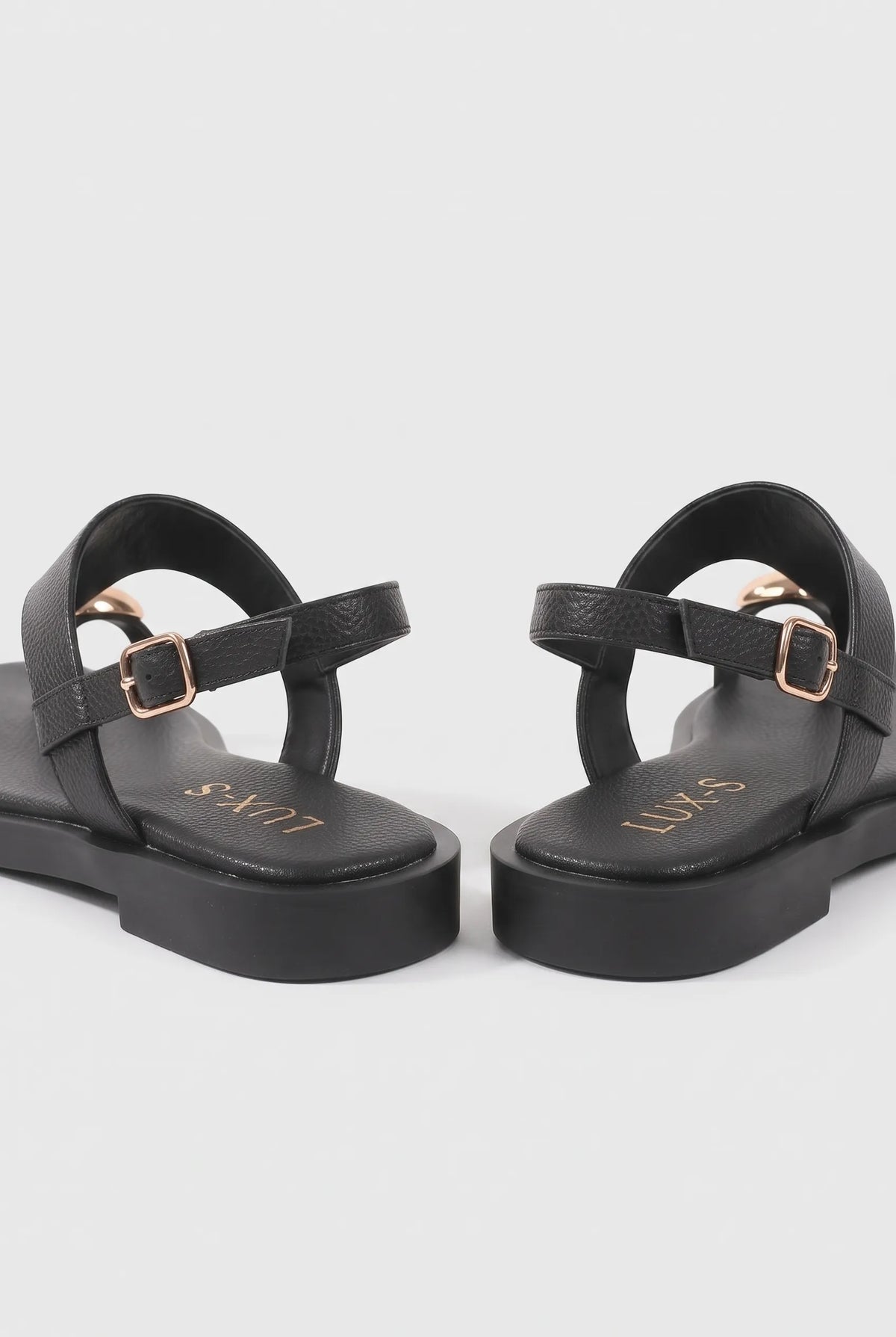 A pair of black platform sandals with double straps and gold-tone buckle details, shown from a side-rear angle on a light gray background.