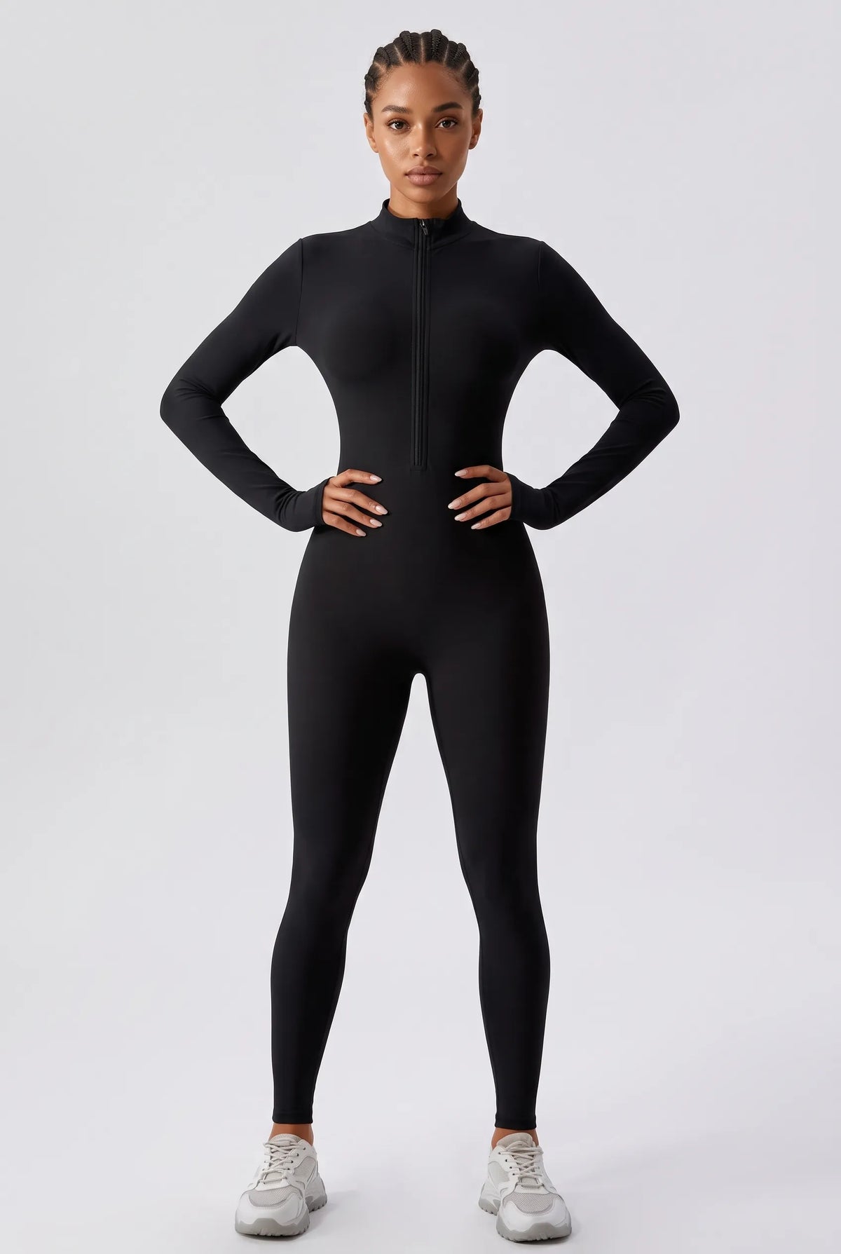 A model wearing a black long-sleeve full-zip athletic bodysuit or catsuit, paired with light gray sneakers, standing against a light gray studio background.