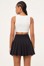 A woman shown from the back wearing a white sleeveless crop top and a black pleated mini skirt, photographed against a plain light background.