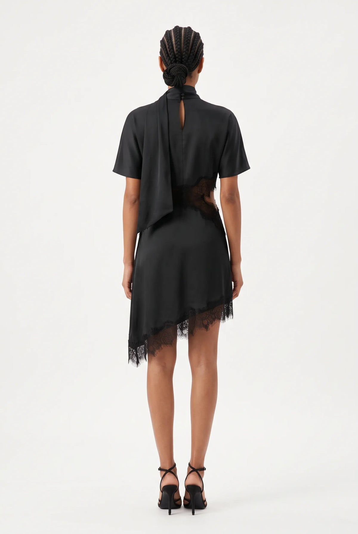 Modern short-sleeved mini dress features an elegant high-neck collar with an attached, long trailing scarf tie that drapes fluidly down the front. Designed with a contemporary midsection cut-out, the edges of the waist, bodice, and asymmetrical hemline are embellished with delicate, intricate eyelash lace trim for a sensual, sheer contrast. The fluid skirt falls into an asymmetrical high-low hem finish, combining structured, high-fashion tailoring with romantic boudoir-inspired details.
