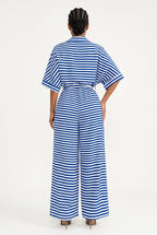 A model viewed from the back wearing a blue and white horizontally striped short-sleeve jumpsuit with a tie waist and wide legs, set against a plain white studio background.