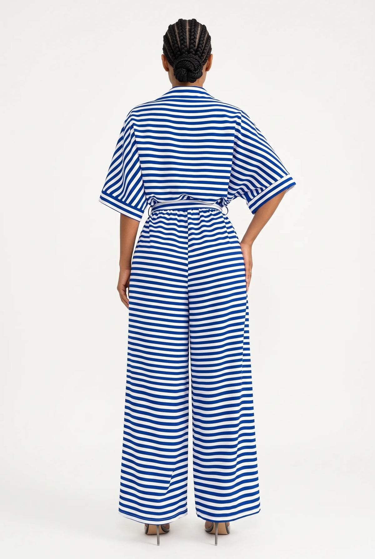 A model viewed from the back wearing a blue and white horizontally striped short-sleeve jumpsuit with a tie waist and wide legs, set against a plain white studio background.
