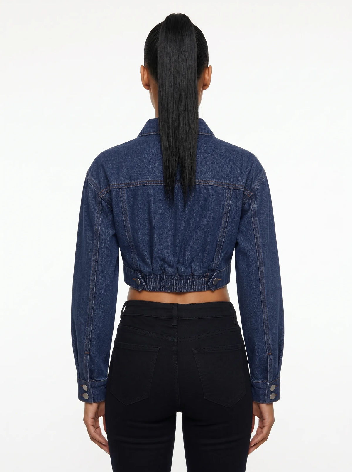 This is a deep indigo blue denim jacket features an ultra-cropped silhouette with long sleeves, tailored shoulder seams, and classic buttoned cuffs. It includes a traditional point collar and a full front placket detailed with smooth, metallic silver shank buttons.